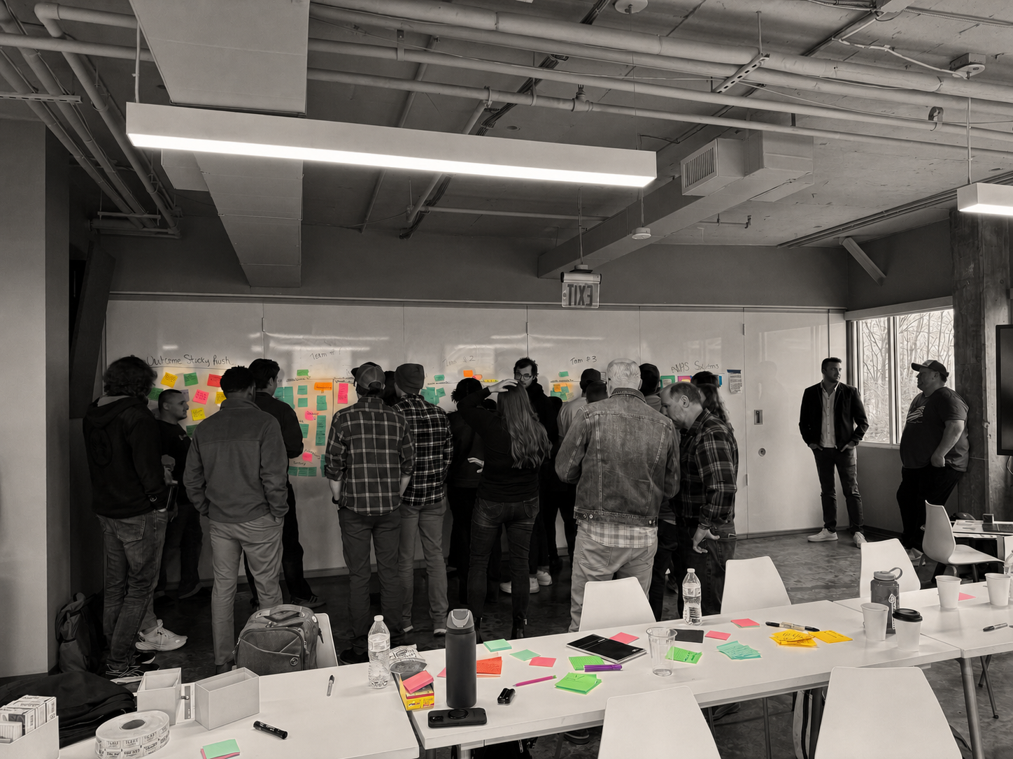 Workshop participants in warm monochrome gathering around a wall and tables filled with illuminated colorful notes